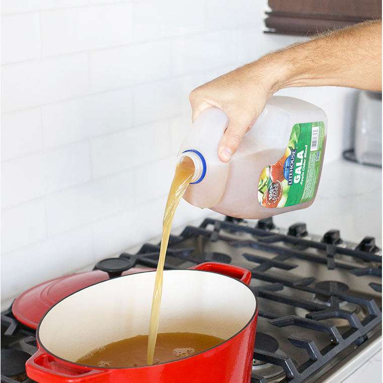 Pouring apple cider into red dutch oven